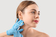 Beautiful young woman receiving filler injection in face on grey background