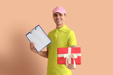 Wall Mural - Male courier with gift box and clipboard on beige background