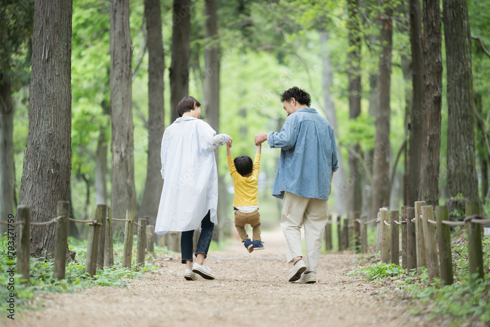 A family walking in good harmony, smiling and holding hands through fresh greenery and beautiful ...