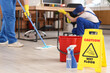 © Pixel-Shot - Caution sign with bottles of detergent and bucket on floor in office, closeup