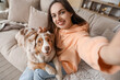 Young woman with cute fluffy Australian Shepherd dog taking selfie in living room
