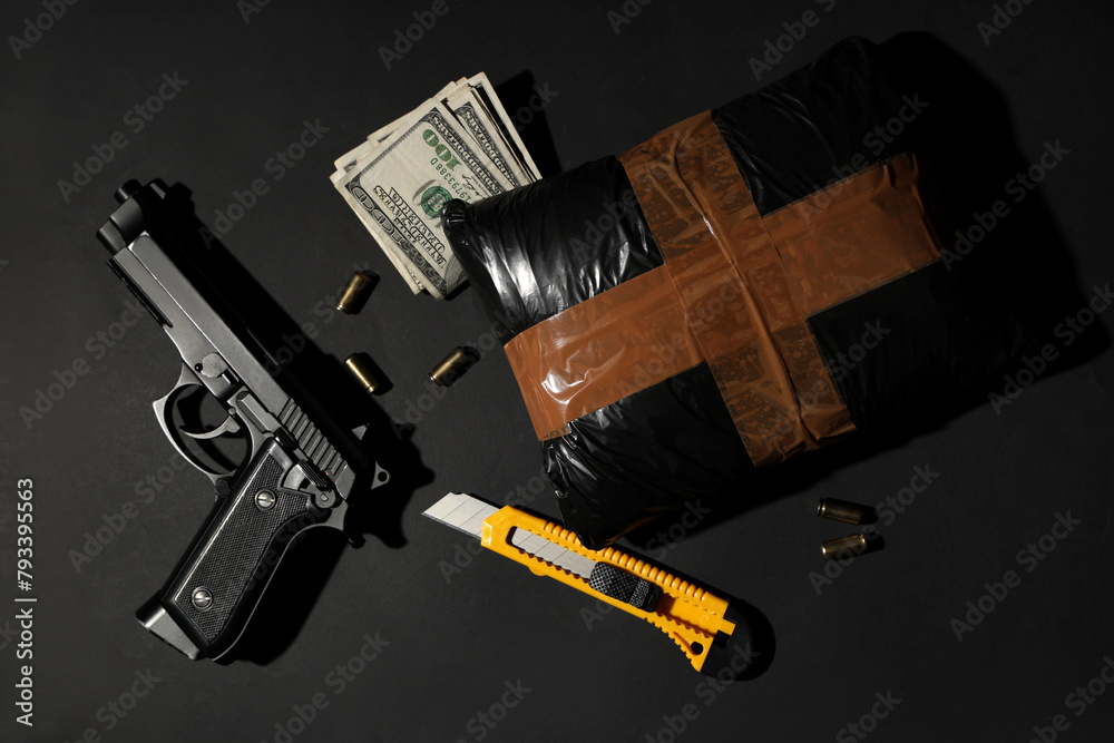 Drug package with gun, money and utility knife on dark background