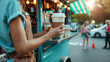 © Kanlayarawit - A happy coffee shop owner standing beside a green food truck is holding a cup of hot coffee to send to a client.