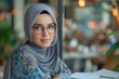 Stylish Muslim Woman with Glasses in a Coffee Shop. Stylish young Muslim woman wearing glasses and a hijab, thoughtfully looking away in a bustling coffee shop.