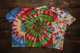 Fototapeta Most - Three bright tie dye T-shirts on a wooden background.