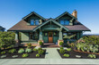 A front view of a striking emerald green craftsman cottage style home, with a triple pitched roof, expertly designed landscaping, 