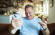 © Marko Geber - Middle Aged Caucasian man using smartphone on the sofa at home