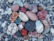 Pile of colorful pebble stones and rocks on sea beach background. Different multicolor pebble stones (green, orange, red, grey, black) pattern. Heap pebble stone texture. Close up pebble stones coast.