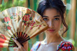 coy demure Asian woman holding decorative bamboo fan to her face