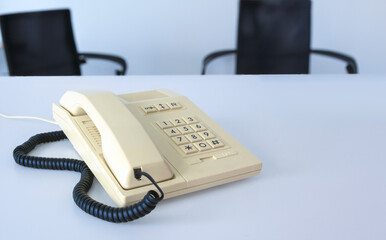 A white phone 80s - 90s with a cord hanging off it sits on a table in office