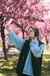 happy woman listening music in headset outdoors taking selfie with sakura on background