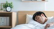 Relaxed guy lying up in comfortable cozy bed wearing white t-shirt, sleeping or napping with eyes closed, holding hands behind the head, resting after working day or waking up in the morning