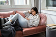 © Cavan Images - Young woman lying on coach in comfy clothes and scrolling on the phone