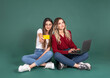 Online shopping, full body sitting two female friends online shopping concept idea image. Showing bank credit debit card to camera, using holding laptop. Studio image of two beautiful women shopper.