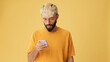 Guy with glasses, dressed in yellow T-shirt, with phone in his hands, surprised, wow effect, isolated on yellow background in studio