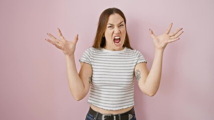 Poster - Young woman with blue eyes unleashing frustration, mad shouting, crazy expression and raised arms over isolated pink background