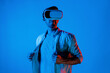 Caucasian man with VR goggle while adjusting casual cloth at neon background. Smiling teenager standing while enter in metaverse or virtual world by using technology innovation simulation. Deviation.