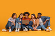 © Prostock-studio - Multiethnic friends looking at laptop together on orange background