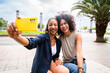 Two mixed race hispanic women bonding outdoors and taking selfie with smartphone for social media