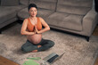 A relaxed pregnant woman meditating at home and following a meditation tutorial on her laptop in the living room