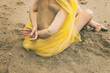 woman covered with a yellow tulle sitting on the sand of an Asturian beach