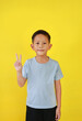Portrait of Asian boy child show victory sign fingers and looking straight while standing isolated on yellow background.