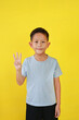 Portrait of Asian boy child show three fingers and looking straight while standing isolated on yellow background.
