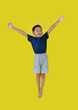 Happy Asian little boy child jumping in air over yellow studio background.