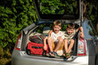Two cute boys sitting in a car trunk before going on vacations with their parents. Two kids looking forward for a road trip or travel. Summer break at school. Family travel by car