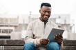 African man, tablet and stairs in city with reading, laughing and happy for comic meme on social media. Person, digital touchscreen and smile for funny video, post or contact on app on steps in metro