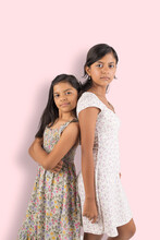 Two Young Girls Are Standing Next To Each Other, One Wearing A Floral Dress
