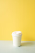 Disposable paper coffee cup on gray table. yellow wall background