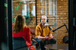  A gathering of young business professionals, some seated in a glass-walled office, engage in a lively conversation and record an online podcast, embodying modern collaboration and dynamic interaction
