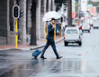 Businessman, walking and city with umbrella on street for travel, work or business trip in winter. Man, employee or pedestrian crossing road with luggage for commute or immigration in an urban town
