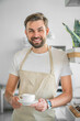 Vertical shot of happy coffee shop owner posing with a coffee cup in hand. Closeup of barista standing at the entrance of coffee shop holding a coffee cup. Food and beverages industry concept