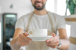 Closeup of barista offering a coffee cup. Coffee shop owner serving coffee. Cropped photo of decaf sugar free non-lactose milk hot beverage cacao chocolate in cafe restaurant