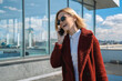 Beautiful caucasian woman walking along in the city and talking on mobile phone. Stylish female model with sunglasses walking on city building terrace and using phone. Businesswoman on conversation