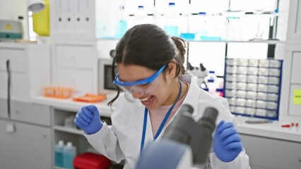 Canvas Print - Elated young hispanic female scientist exults her mad win in the lab, delightedly celebrating an exciting success with arms raised, wearing safety glasses