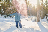 Fototapeta  - Ecstatic boy in blue warm winterwear standing in snowdrift in park or forest and throwing snow over his head while having fun