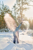 Fototapeta  - Excited kid in winterwear standing in snowdrift in natural environment on sunny winter day and having fun with snow
