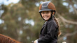 A young rider wearing a horse riding helmet, smiling at the camera while confidently handling the reins during an equitation lesson.