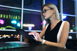 Fully concentrated beautiful young businesswoman with blonde hair glasses spectacles holding tablet in hand sitting on a table at coworking with look in laptop. Female entrepreneur using gadget