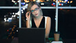 Portrait of young caucasian female executive sitting on a table with coffee cup and laptop on it and looking at camera while working late at office. Businesswoman with her hand on glasses