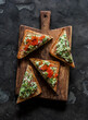 Delicious tapas, appetizer, snack - bruschetta with avocado, eggs, gherkins, greens spread and red caviar on a wooden chopping board on a dark background