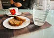 Frau sitzt vor Küchentisch mit Karaffe Wasser, Tasse Kaffee und Bananenbrotscheiben auf weißem Teller in Küche 