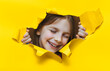 A funny laughing red-haired girl looks out through a hole in yellow paper. The concept of surprise, smile, joyful mood from what he saw. Discounts, sales, surprise. Copy space.