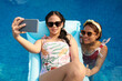 © DragonImages - Teenage girl relaxing on inflatable mattress and taking selfie with mother