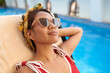 © DragonImages - Portrait of smiling woman in sunglasses sunbathing by swimming pool