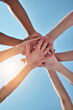 People, team and hands together below for unity, collaboration or synergy on a blue sky background. Closeup or low angle of group or community piling or stacking in solidarity for join or mission