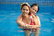 © DragonImages - Girl hugging mother from behind when they are swimming in pool